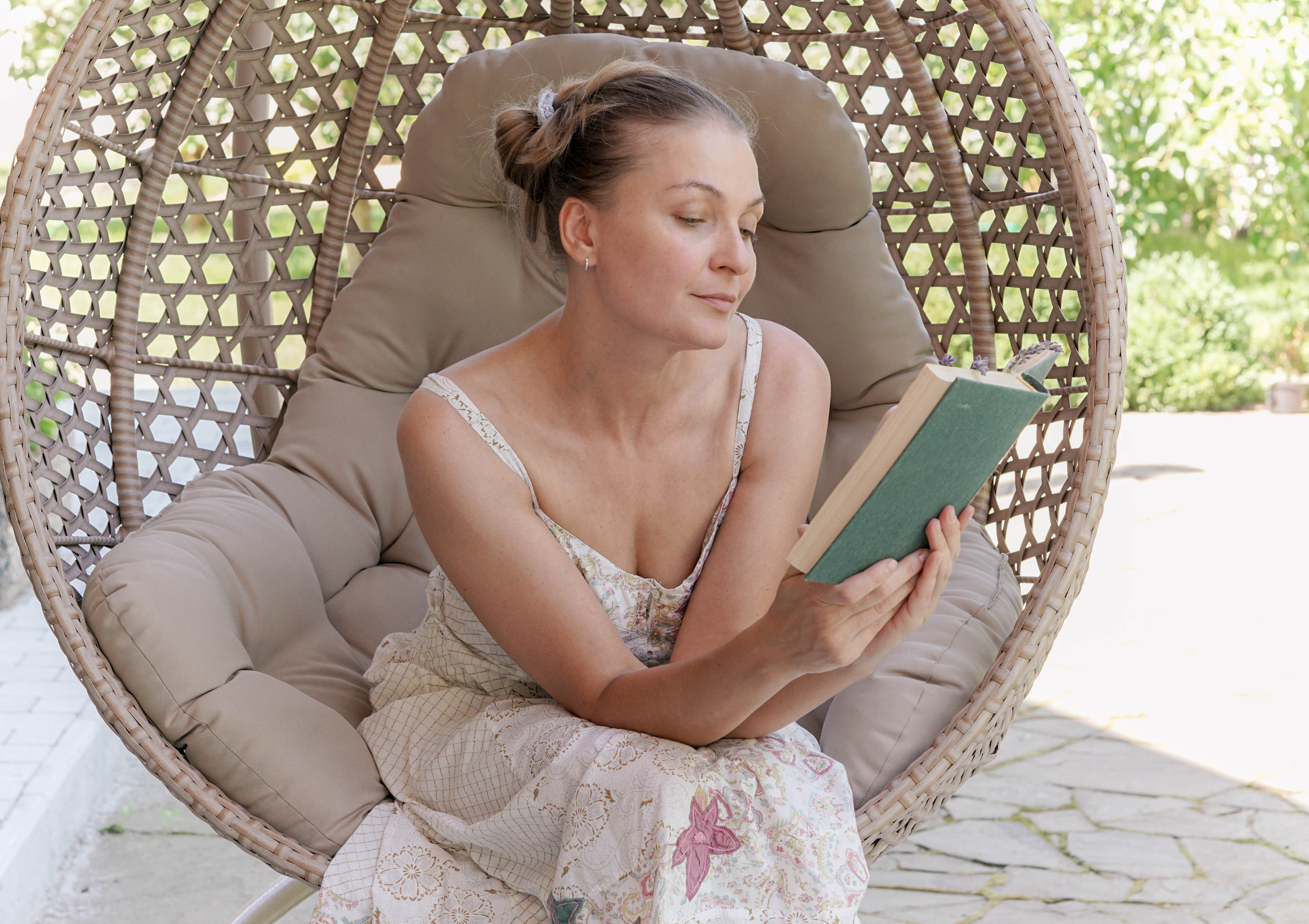 A woman sitting in a chair cocoon and reading a book