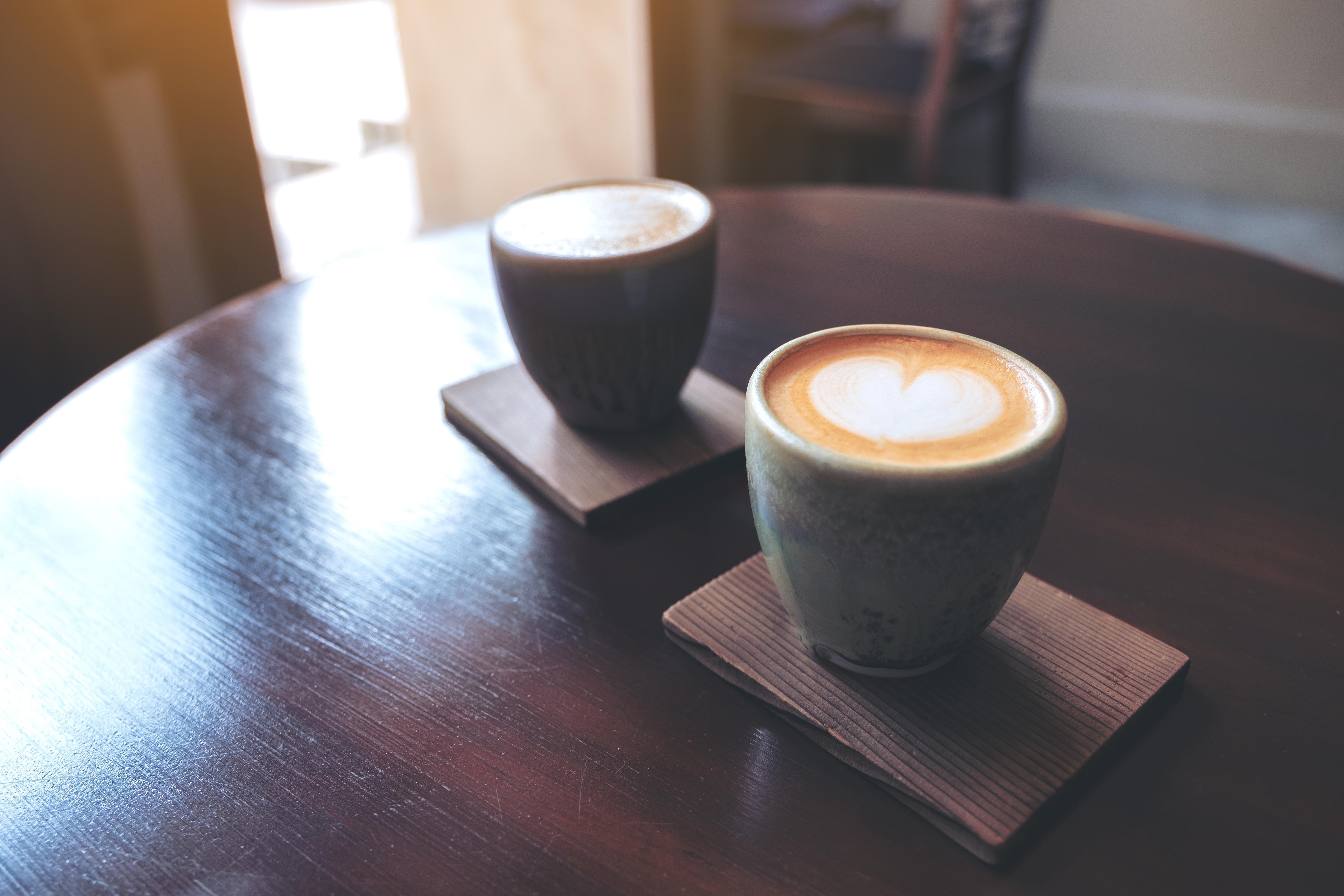 Closeup image of two small cups of hot latte coffee with latte art on vintage wooden table in cafe