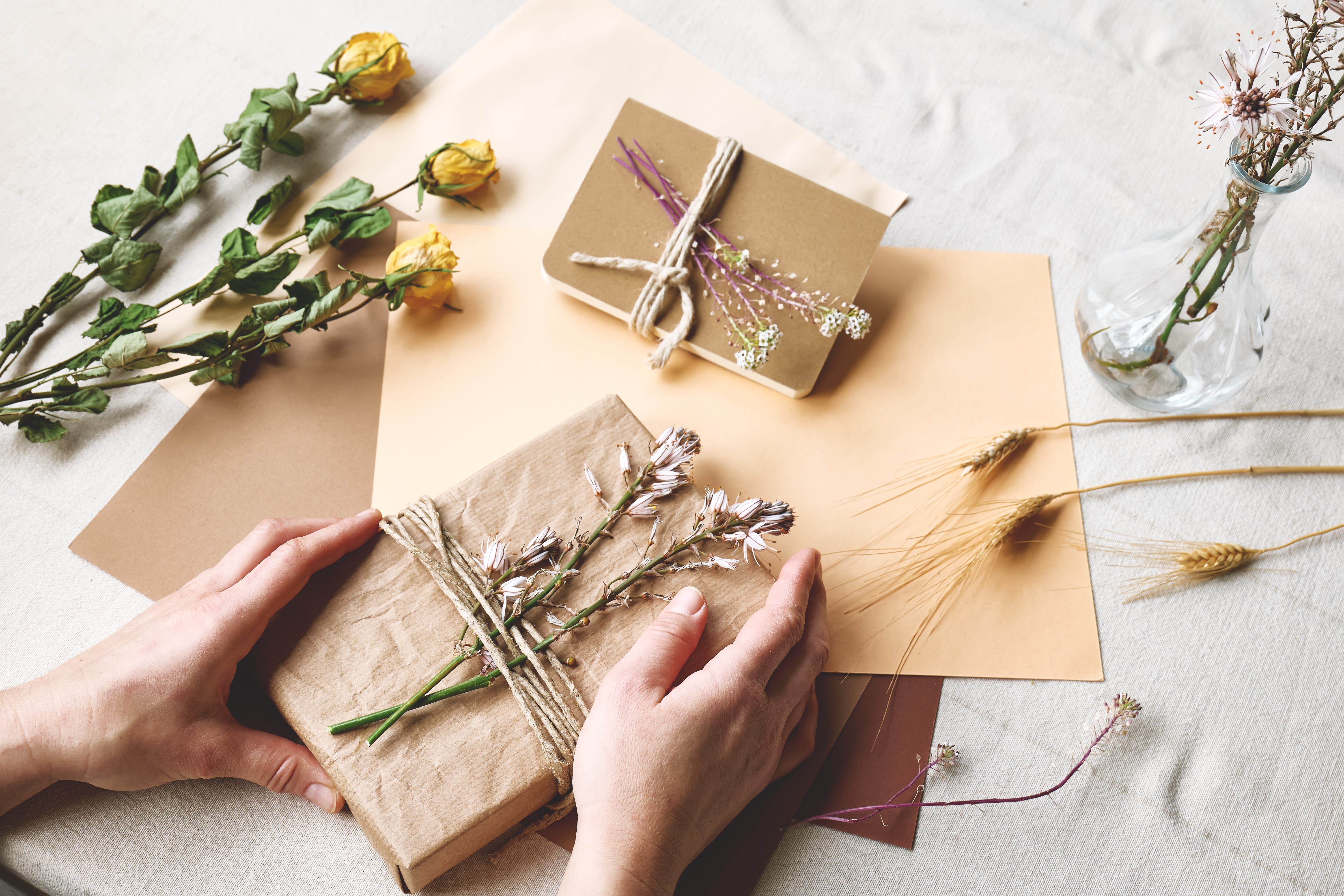 Woman makes zero waste, trendy handmade gift package with craft recycled paper and dried flowers.
